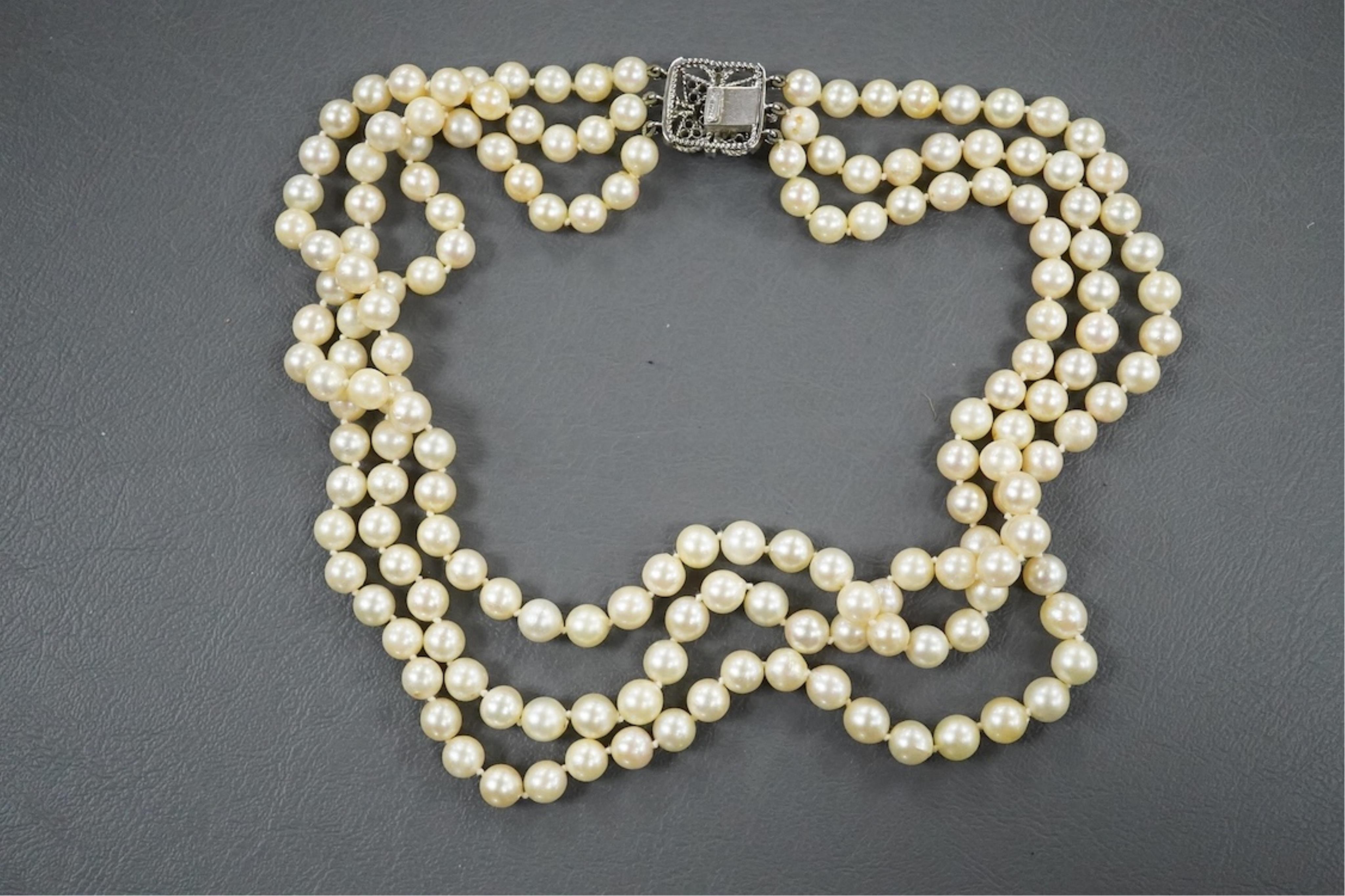 A triple strand cultured pearl necklace, with an Italian 18k white metal, ruby, sapphire and emerald set clasp, 46cm.